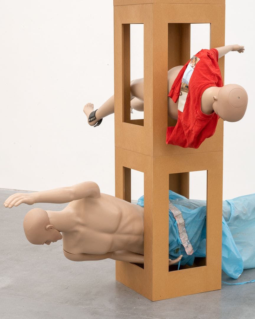 A detail view of an untitled MDF tower, mannequins, leather, plastic tape, hospital gown, jumper with transfer print, and jumper sculpture by Isa Genzken, dated 2018.